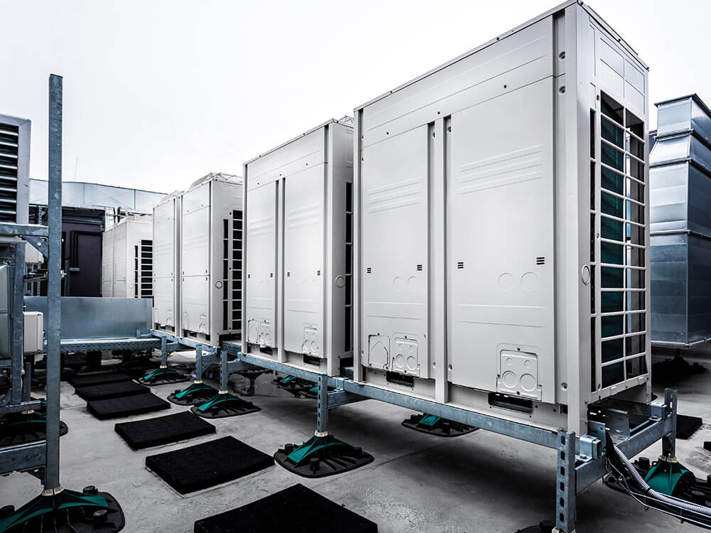Commercial rooftop HVAC units installed on metal mounting racks, connected to ductwork and positioned on protective pads.