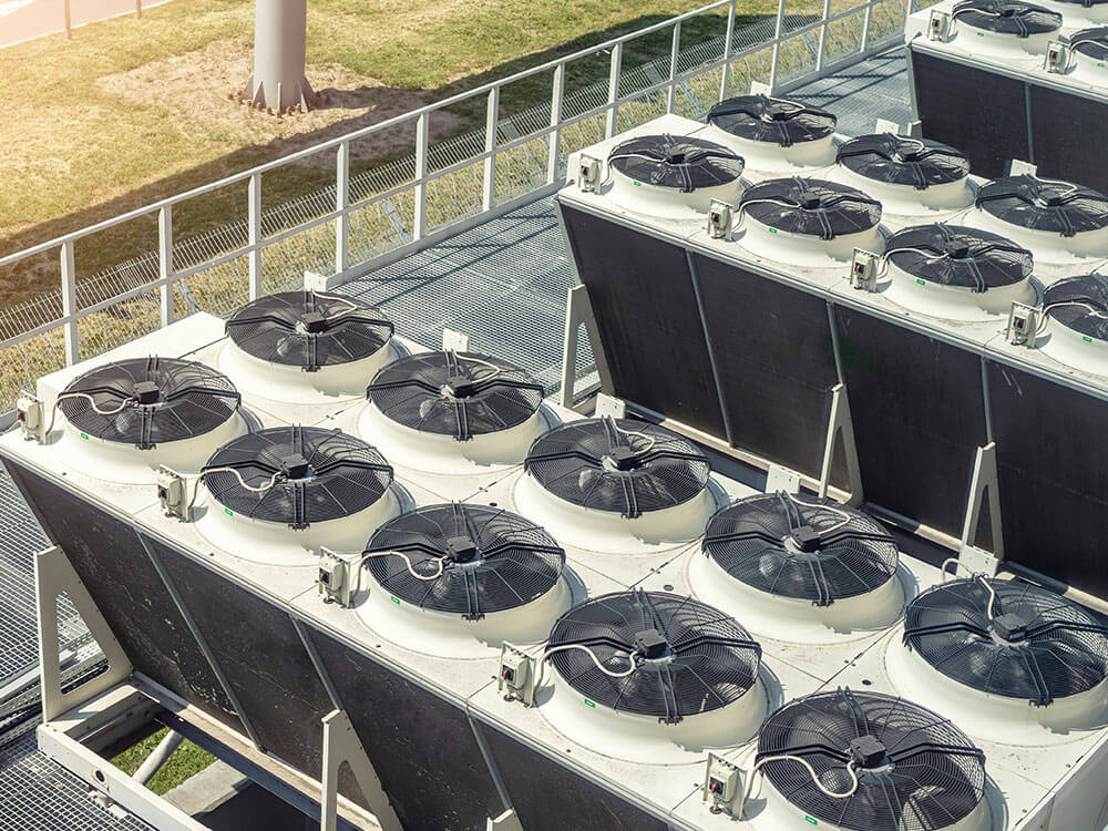 Large commercial HVAC cooling units installed outdoors, with rows of industrial condenser fans positioned on metal platforms above ground level.